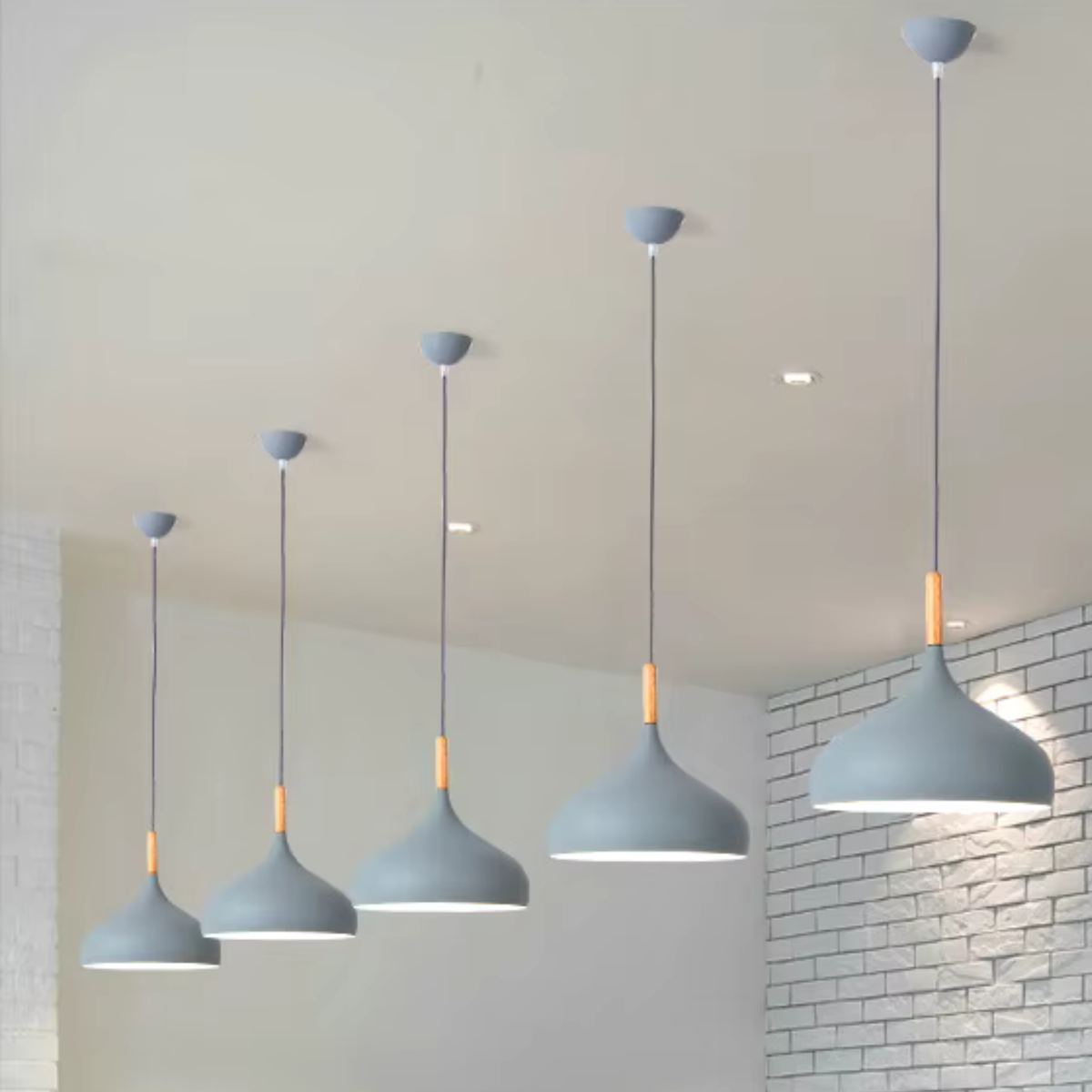 Row of four grey dome pendant lights with wooden fittings hanging at different heights in a modern interior with brick wall - Nordic pendant lights - Litora