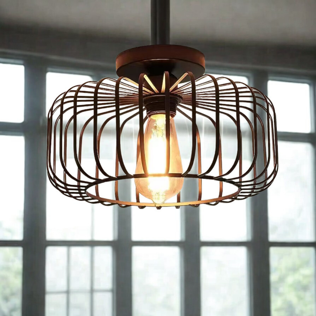Black round wire cage ceiling light with glowing Edison bulb installed in front of large factory windows - industrial semi-flush light - Litora